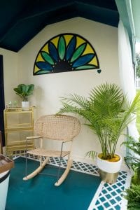 Shed detail: Rocking chair next to potted plant. Wall art of blue and green flower.