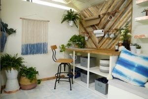 Shed detail: Wooden table top and tall chair. Plants and rolls of material on wall.