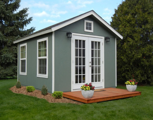 Gym or yoga studio She Shed: Exterior of dark green shed with small patio and flower pots.